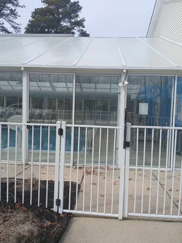 Commercial pool enclosure exterior with white aluminum sliding glass doors and safety fence